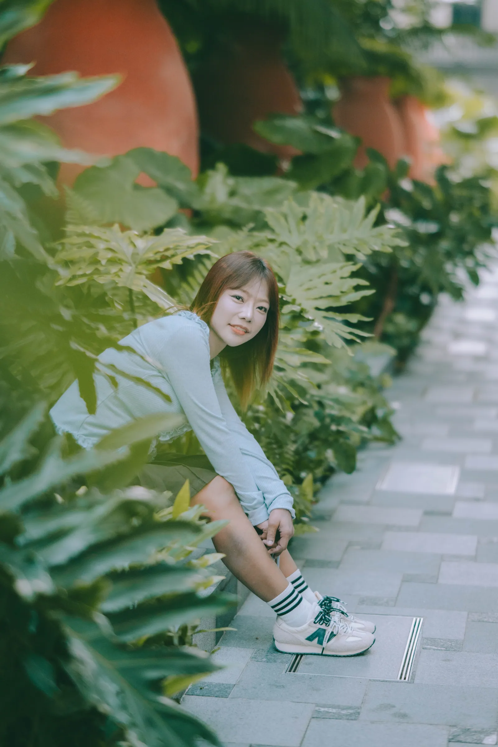 Woman sitting among tropical plants beside large terracotta pots, birthday photoshoot in Singapore