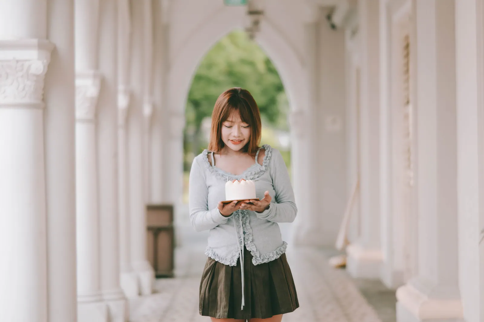 Woman holding a small strawberry birthday cake in a white arched corridor, CHIJMES birthday photoshoot, Singapore