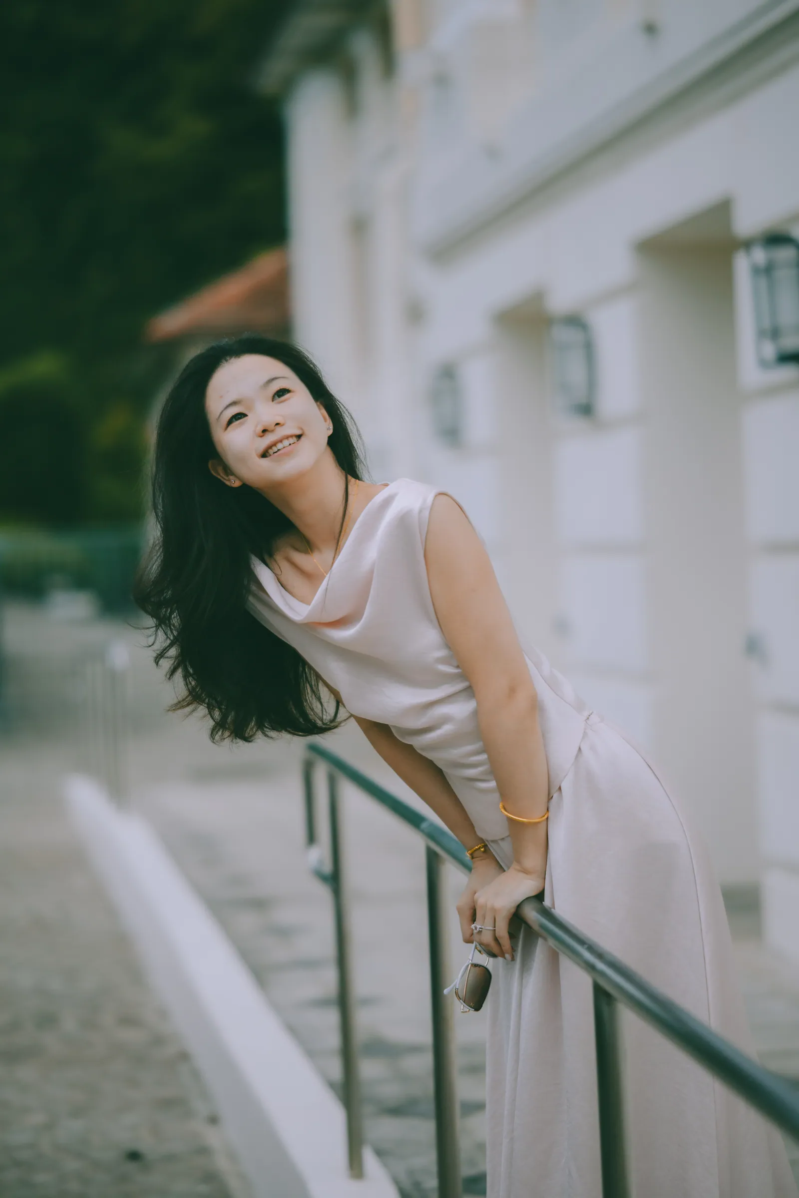 Smiling woman leaning on a railing in front of a white colonial building at Fort Canning Park, Singapore