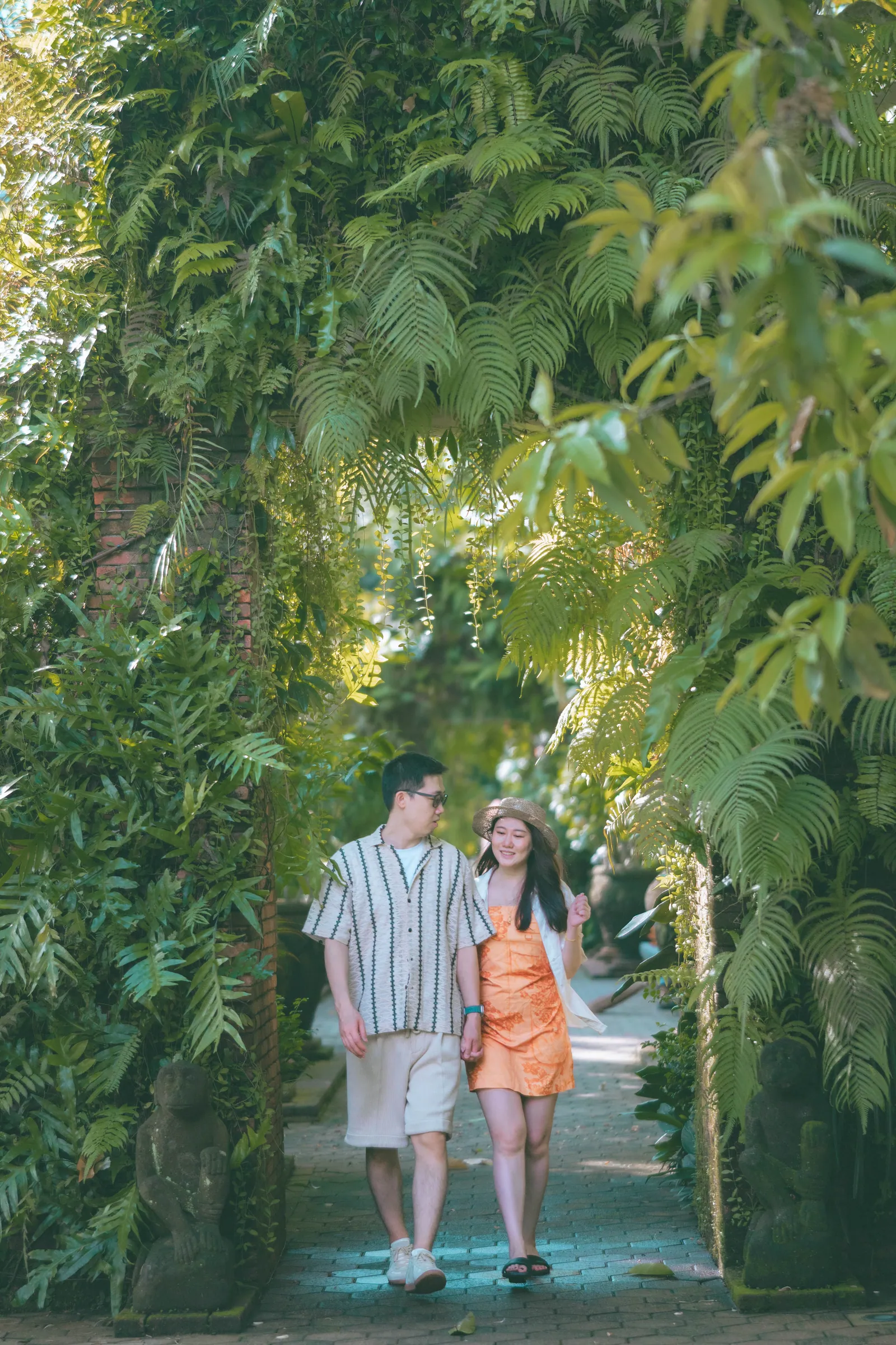 Couple walking hand in hand along a path covered by ferns and tropical plants, Fort Canning Park couple photoshoot