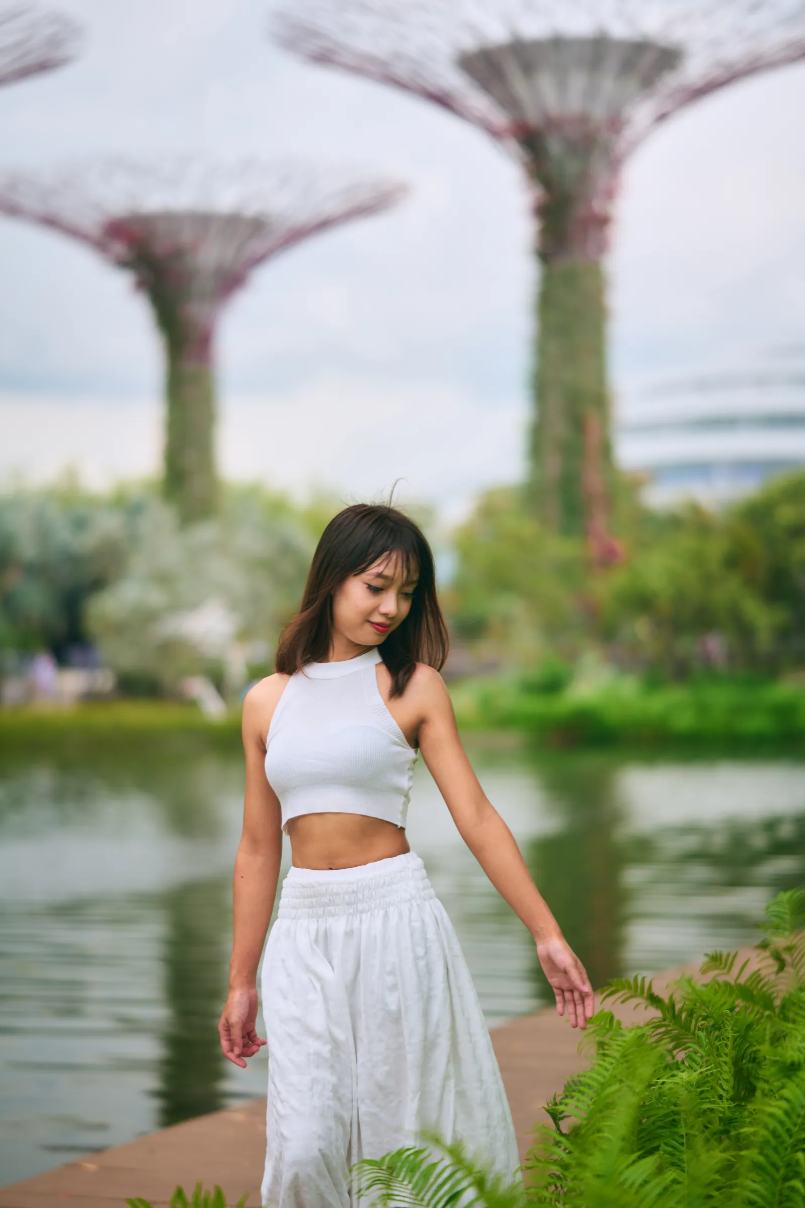 Woman in white walking by the lake with Supertrees softly blurred behind her, Gardens by the Bay