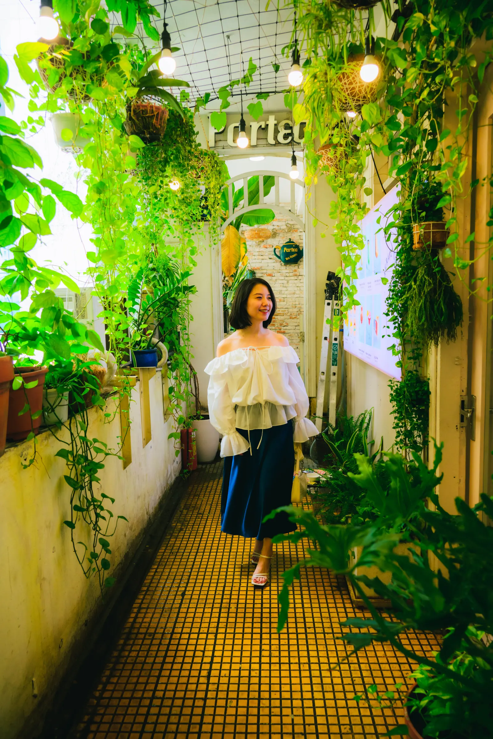 Woman walking through a café corridor full of hanging plants and string lights, Ho Chi Minh City