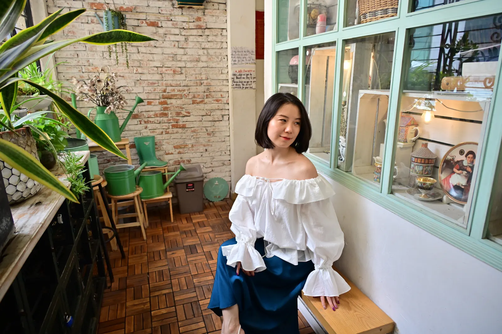 Woman in a white off-shoulder top sitting by a mint-green window in a vintage café, Ho Chi Minh City