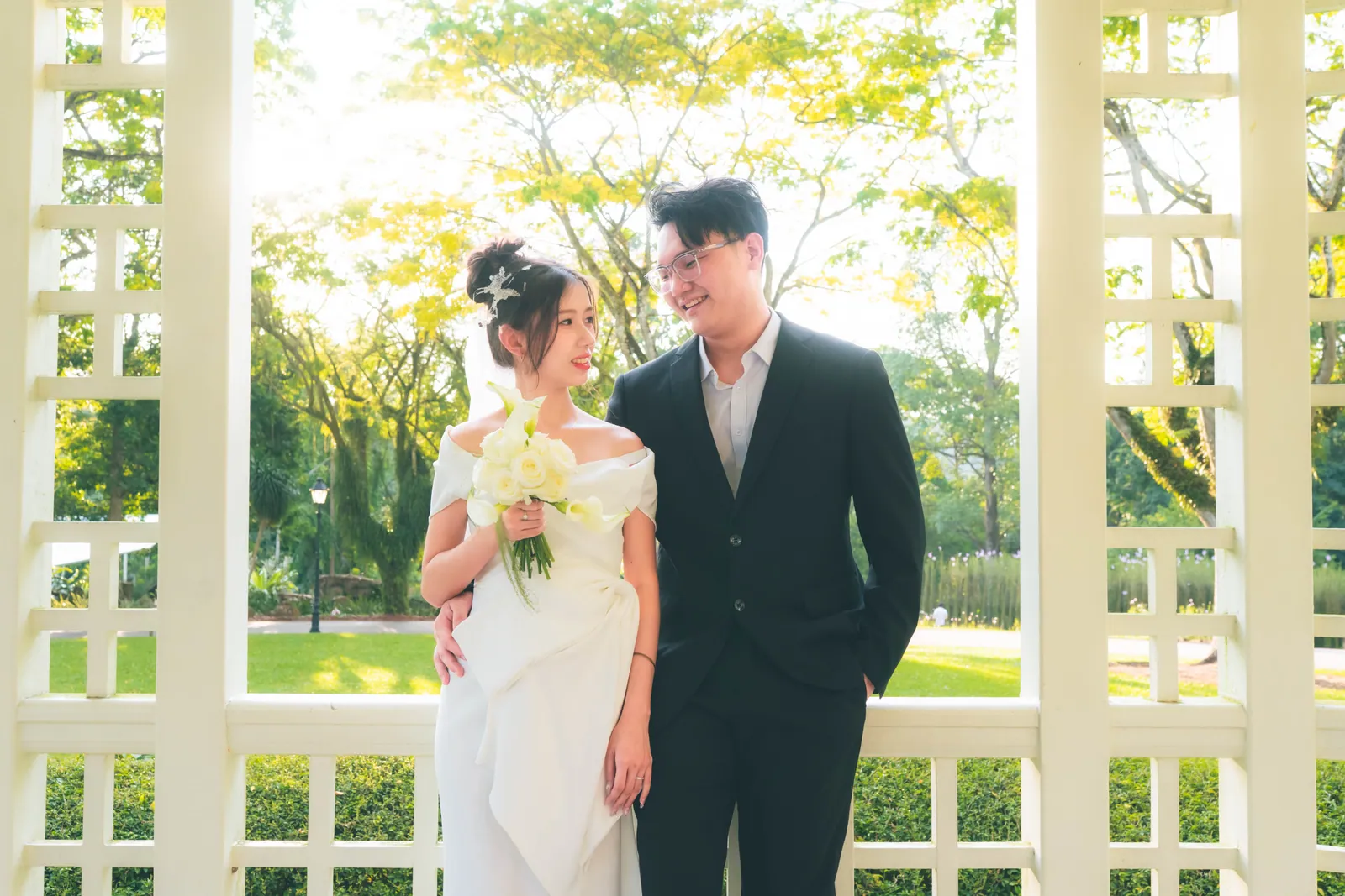 Bride and groom smiling at each other inside the white lattice gazebo, Singapore Botanic Gardens