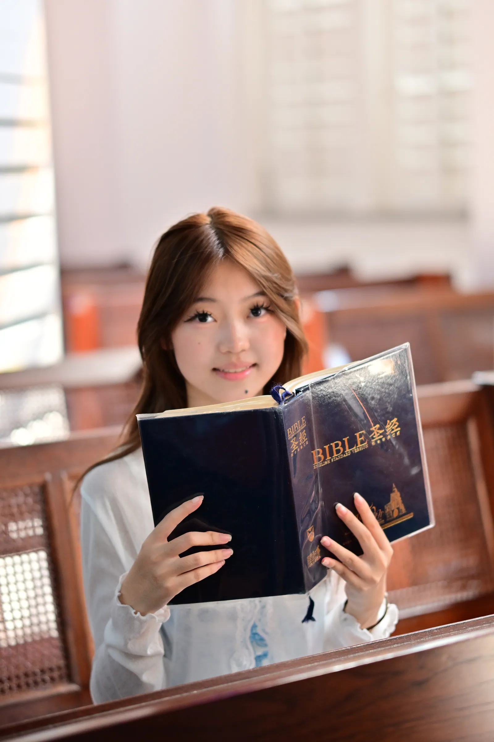 Woman smiling over the top of an open book she holds up in both hands, sitting in a pew at St Andrew's Cathedral, Singapore