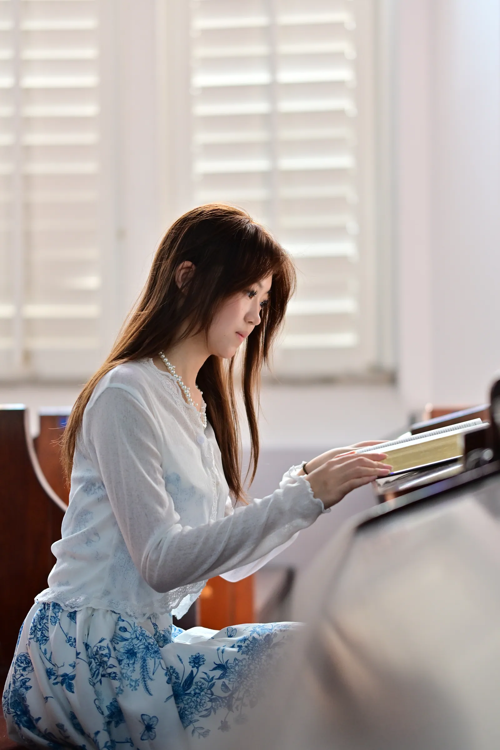 Woman in a white cardigan and pearls reading a book in a wooden pew, lit softly from white louvred windows, St Andrew's Cathedral, Singapore