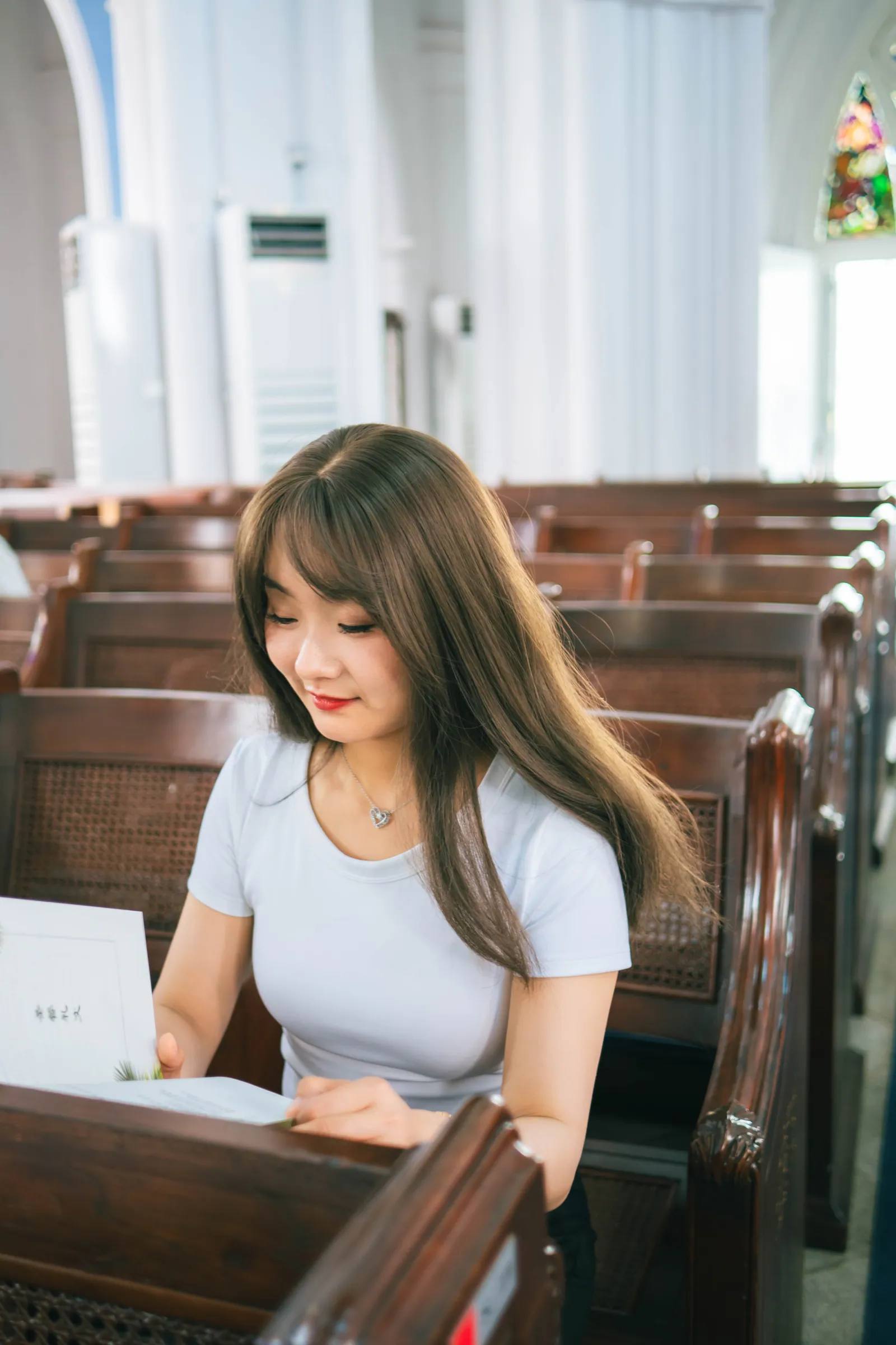 Woman in a white T-shirt sitting in a wooden pew, looking down at a card, inside St Andrew's Cathedral, Singapore